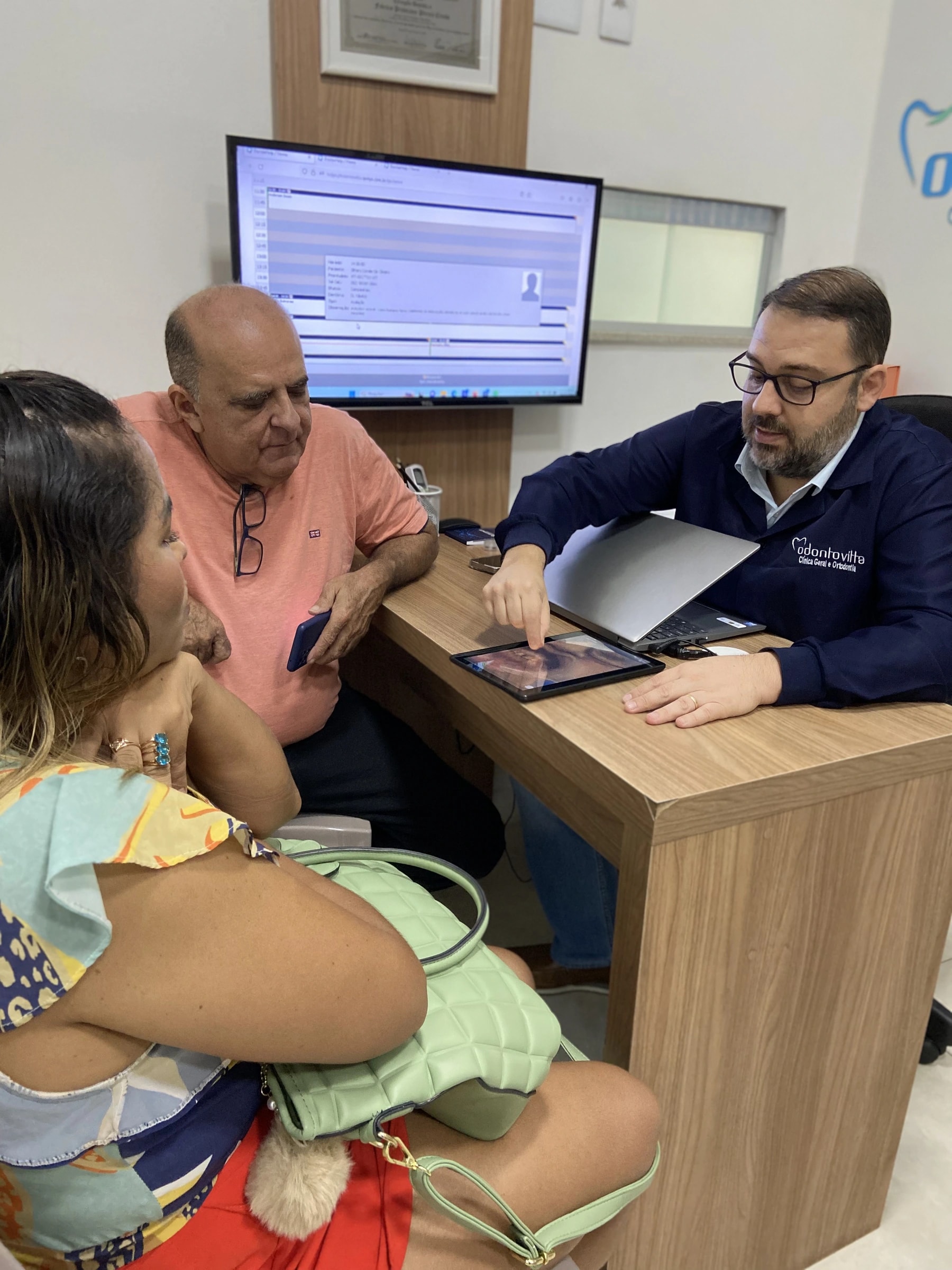 Profissional da Odonto Vitta conversa com pacientes e explica imagens em um tablet
